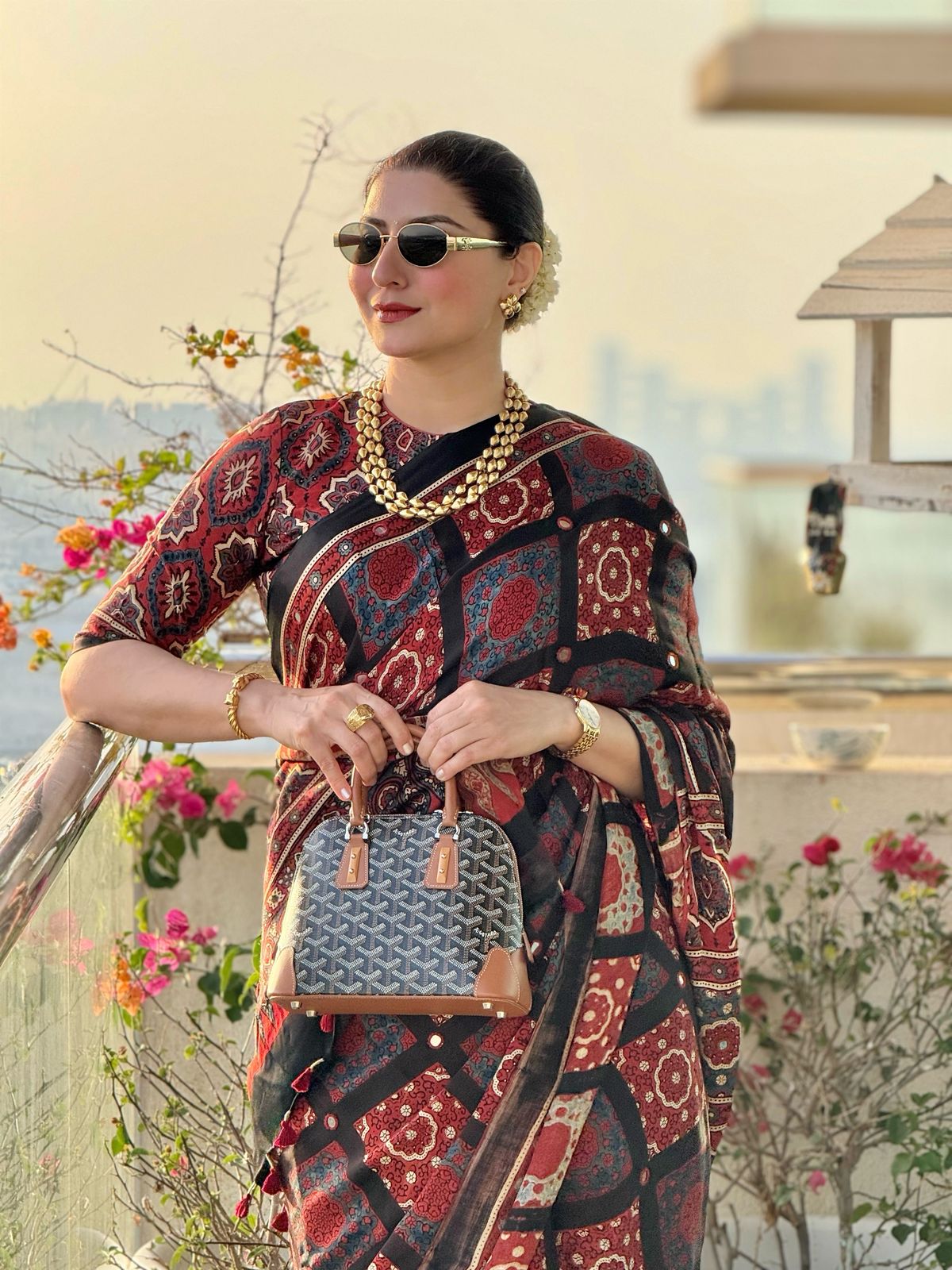 Kawaii floral ajrakh saree worn by woman with gold jewelry and sunglasses carrying handbag